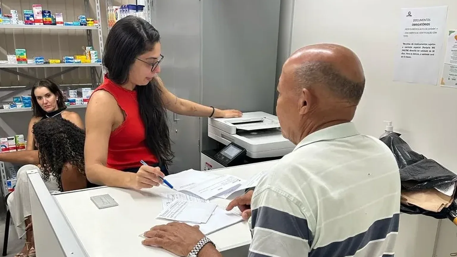 Atendente da Remediar confere a receita no balcão enquanto a pessoa aguarda a retirada do medicamento
